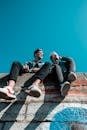 Two young people sitting on a stone wall under a vibrant blue sky, enjoying a sunny day together.