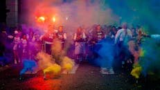 A lively group celebrating at night with color smoke bombs in a street festival.